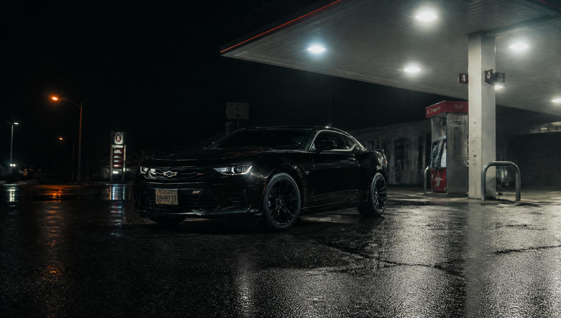 Black performance car parked under gas station lights at night